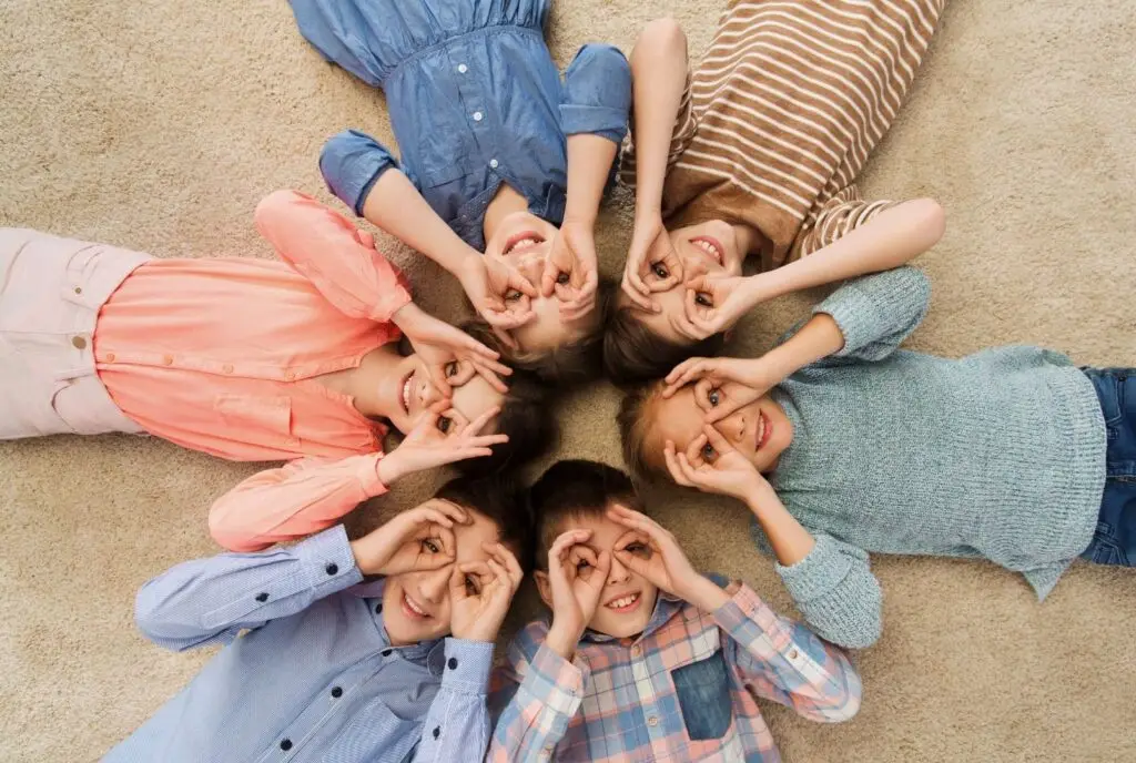 photo d'enfants allongé en formant un cercle, ils entourent leur yeux avec leur main pour faire des lunettes