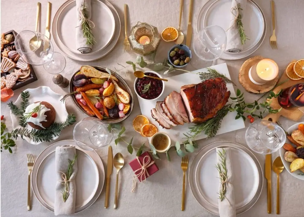 photo d'une table festive décoré avec des branches de sapin et petits cadeaux, 4 couverts sont installés et un rôti est servi au centre de la table
