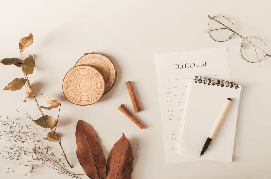 photo d'un carnet à spirale et d'une liste "to do list", des lunettes de vue sont posées au-dessus sur la droite, il y a 2 rondelles de bois et des feuilles d'arbres séchées