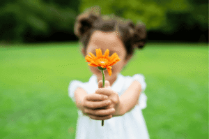 photo floue d'une petite fille tenant à bout de bras une fleur orange nette