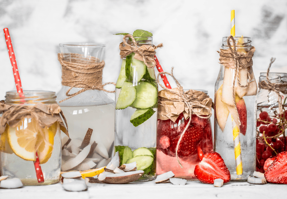 Photo de bouteilles d'eau aromatisée de droite à gauche : rondelle d'orange, copeaux de noix de coco, rondelles de concombre, fraises, fin quartier de pomme et raisins