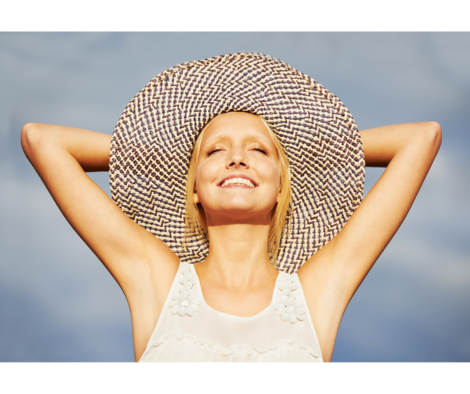 Photo d'une femme souriant les bras derrière son chapeau de paille