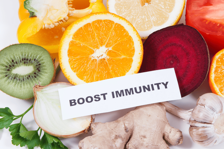 Photo de fruits et légumes coupés en 2. Au centre, une étiquette blanche où il est écrit "Boost Immunity".. Au-dessus : une rondelle d'orange, à droite une tranche de betterave, à gauche une moitié de kiwi. En bas à gauche, une moitié d'oignon et à droite un morceau de gingembre.