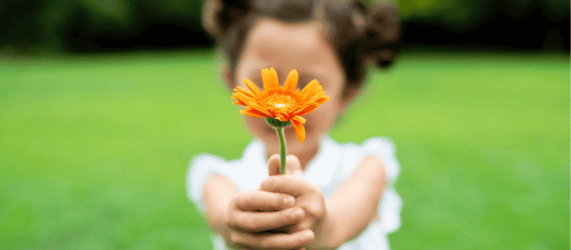 sophrologie-naturopathie-fleur-petit-fille photo floue d'une petite fille tenant Ă  bout de bras une fleur orange nette