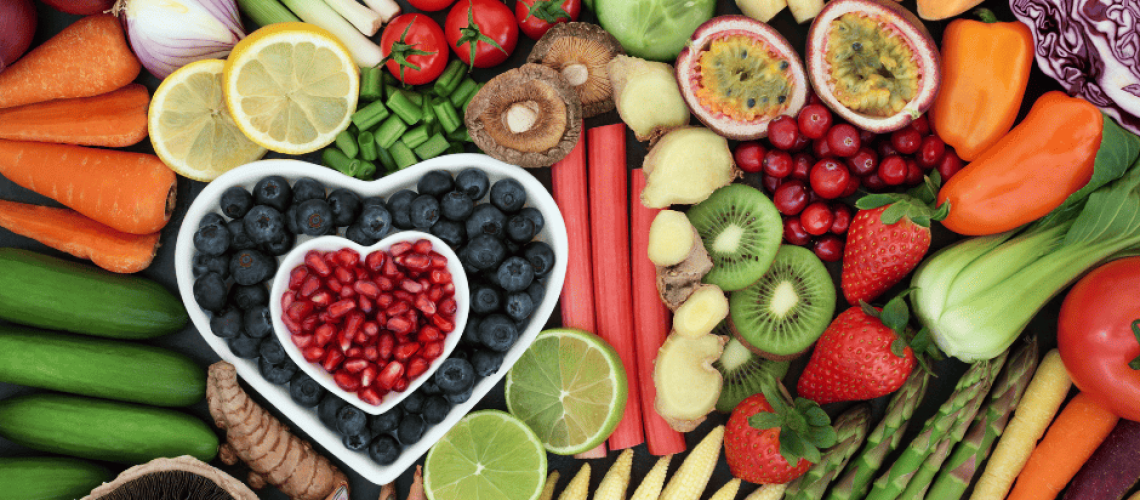 sophrologie-naturopathie-alimentation-Ă©tĂ© photo de fruits et lĂ©gumes de l'Ă©tĂ© avec sur la gauche un plat en forme de coeur de myrtilles, au-dessus un plus petit plat en forme de cĆur contenant des dattes. On voit des rondelles de citron, des asperges, des carottes, des tomates, un comcombre tranchĂ©, des poireaux, des fraises, un kiwi coupĂ© en 2...