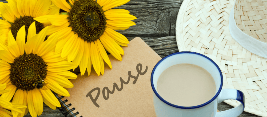 sophrologie-naturopathie-pause photo d'un petit carnet à spiral de couleur carton sur lequel le mot "pause" est écrit. Une tasse d'une boisson chaude est posée en bas à droite. On aperçoit le bout d'un chapeau de paille. En haut à gauche, il y a une fleur de tournesol.